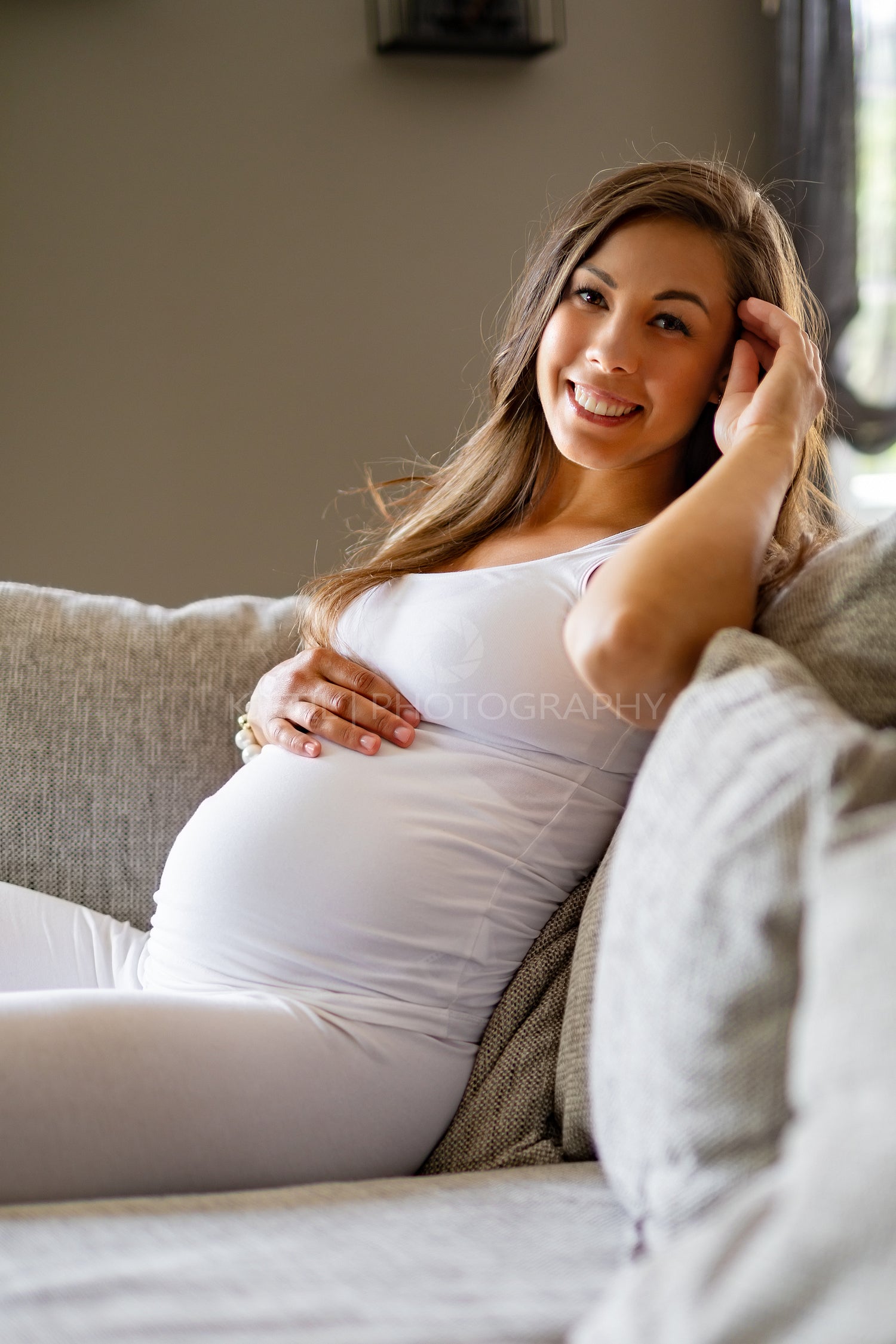 Happy beautiful pregnant woman sitting in sofa touching her belly