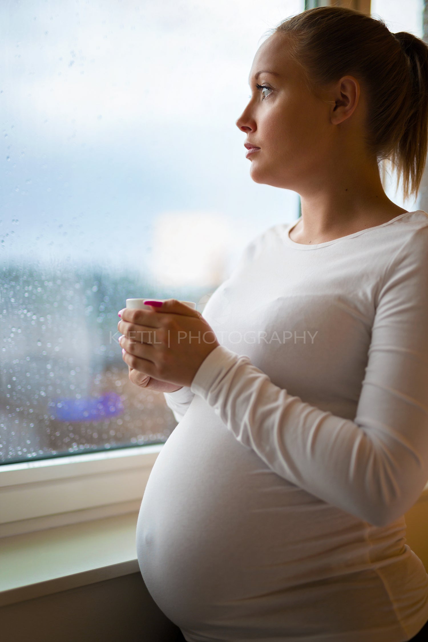 Thoughtful pregnant woman looking out the window drinkng tea