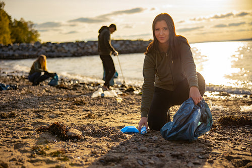 Focused young woman cleaning beach with a team of volunteers during sunset