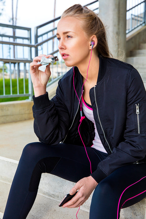 Sporty Woman Eating Protein Bar While Listening Music On Steps