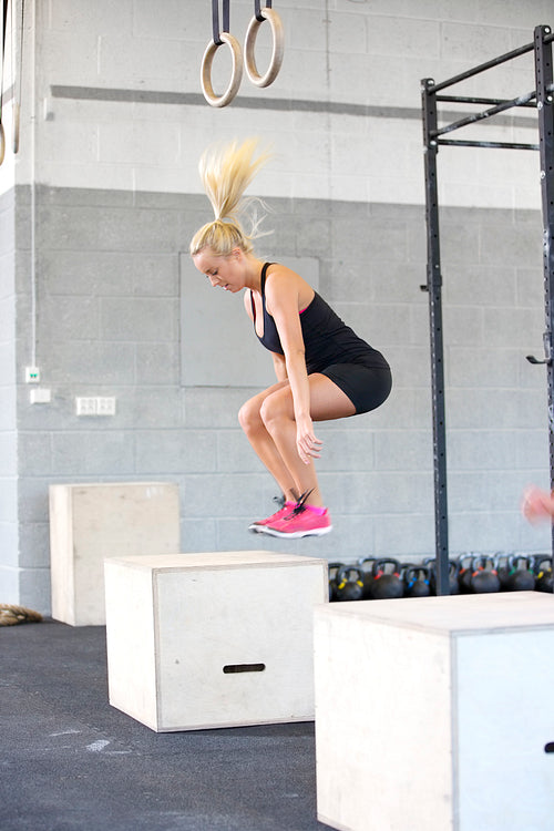 Fit young woman box jumping at the fitness gym