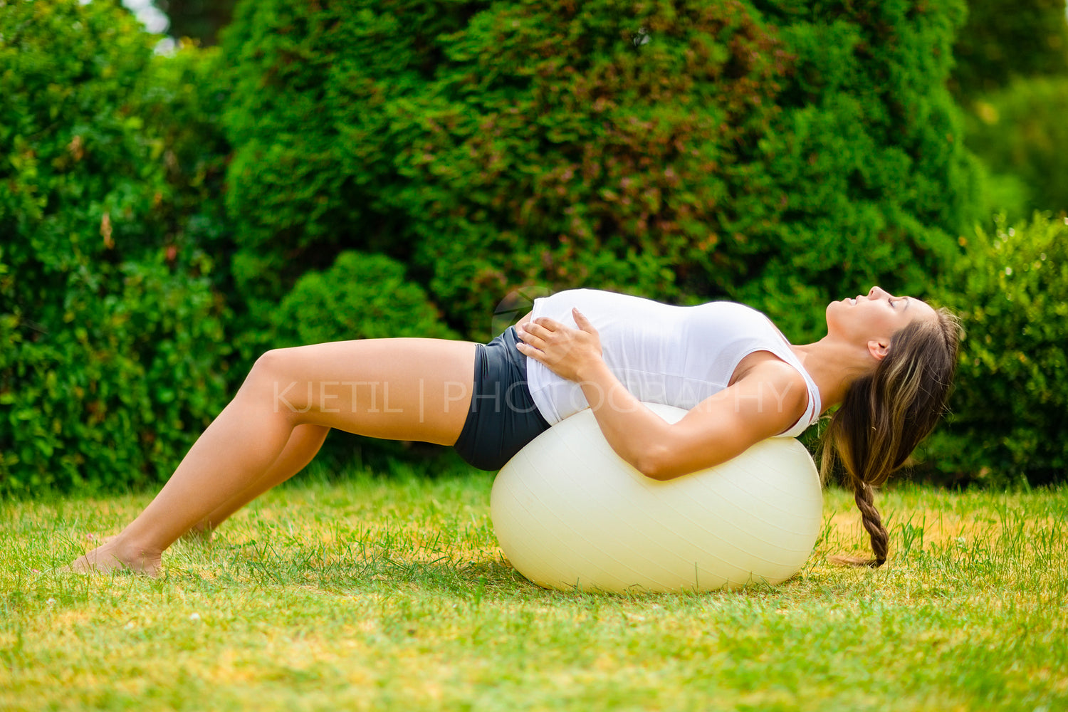 Pregnant Woman Stretching Back On Yoga Ball In Park