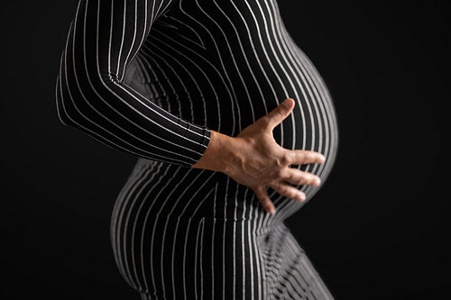 Pregnant Woman Holding Hands on Belly in Striped Dress with Black Background