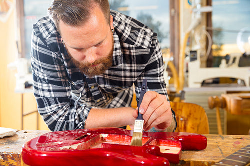 Craftsman with beard working at workshop with a guitar restoration