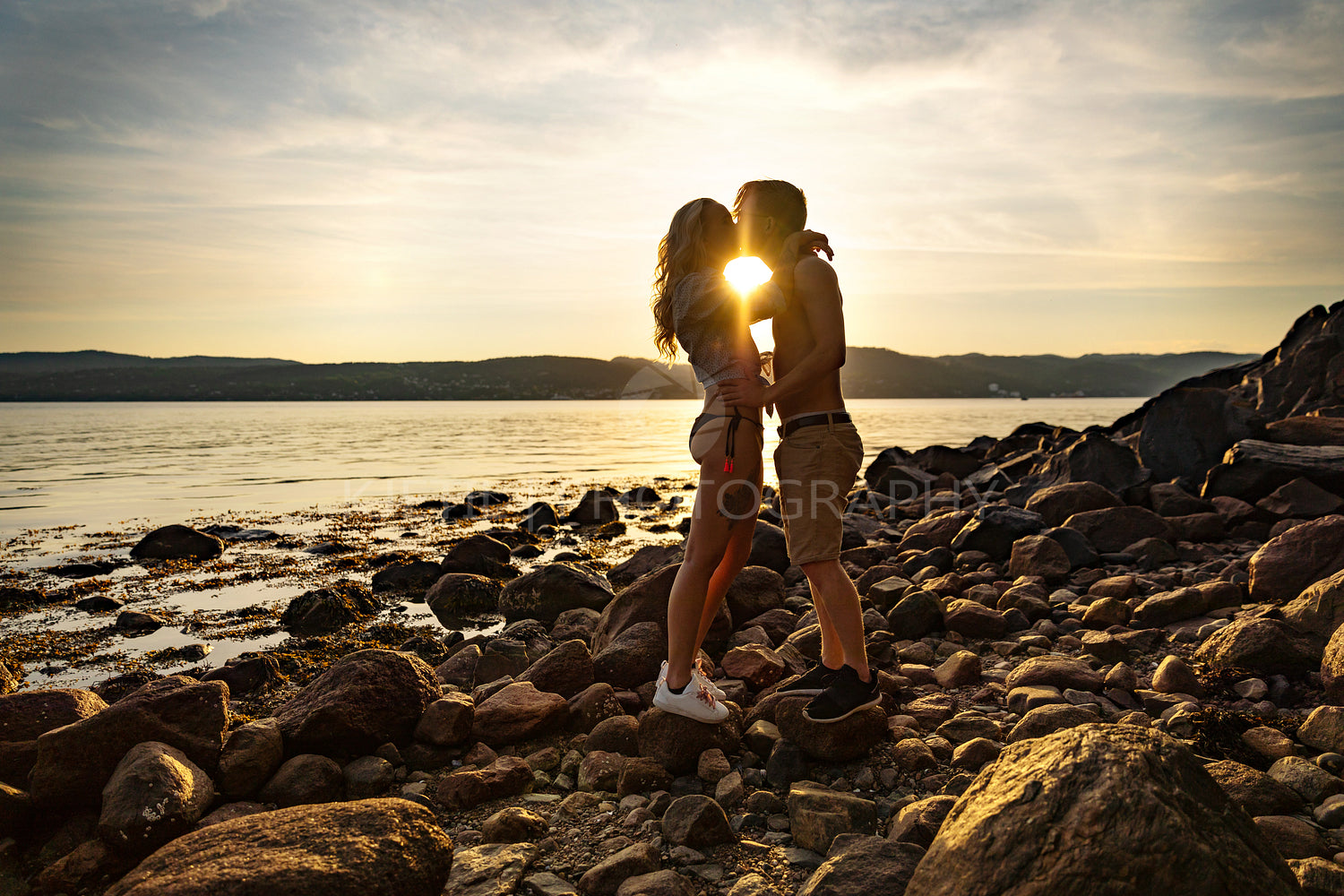 Silhouette of couple in love embracing at the beach against sun