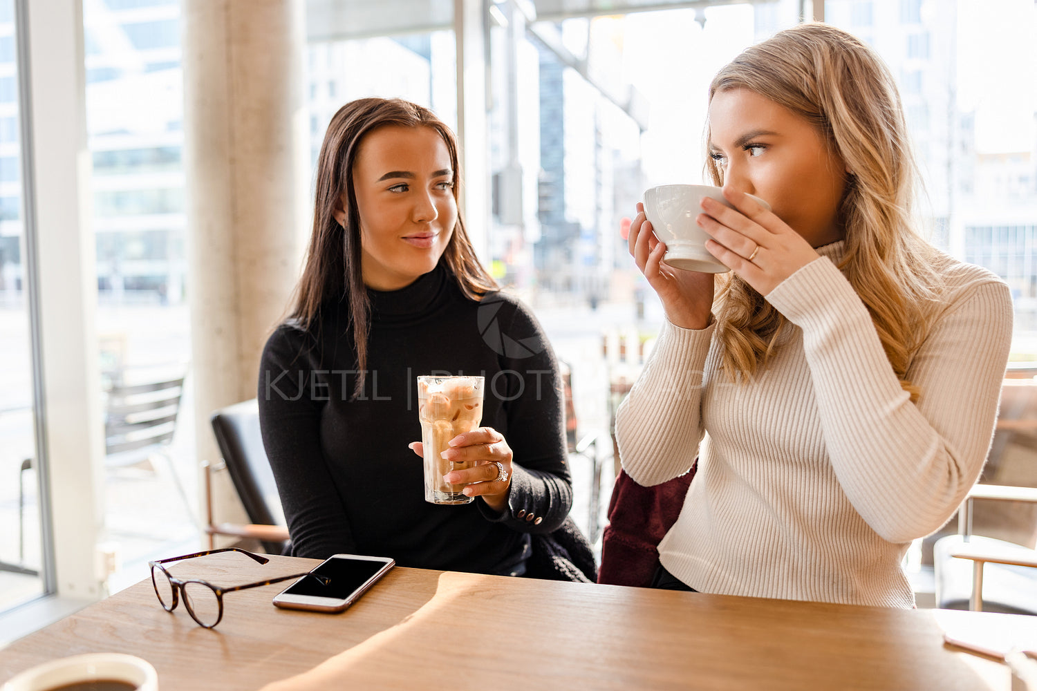 Smiling Women Talking and Drinking Coffee At Modern Cafe in City