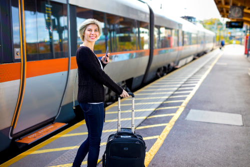 Happy Woman With Mobile Phone And Luggage At Train Station