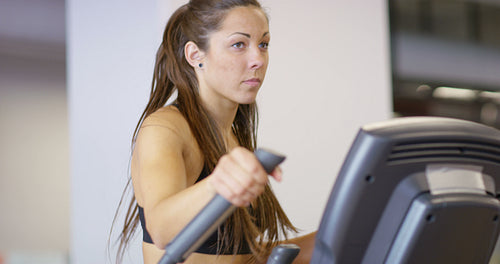 Fit woman training on ellipse exercise machine in fitness gym