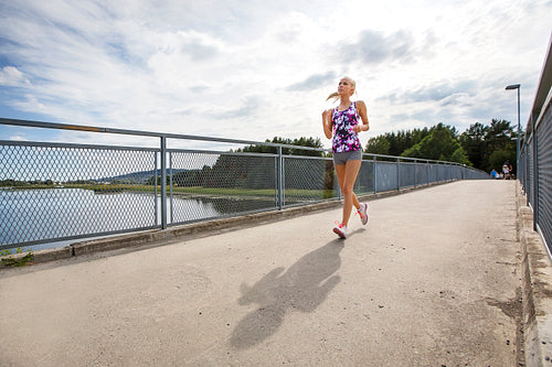 Running woman jogs in sunshine outdoor on bridge