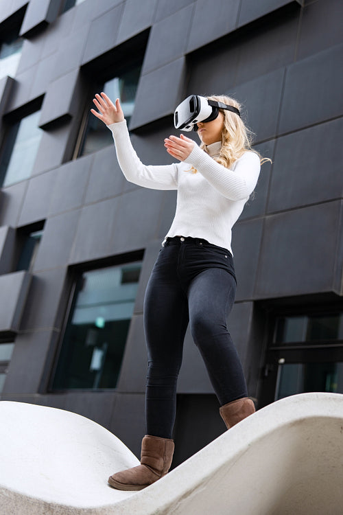 Woman Wearing Virtual Reality Glasses In Front Of Futuristic City Building Wall