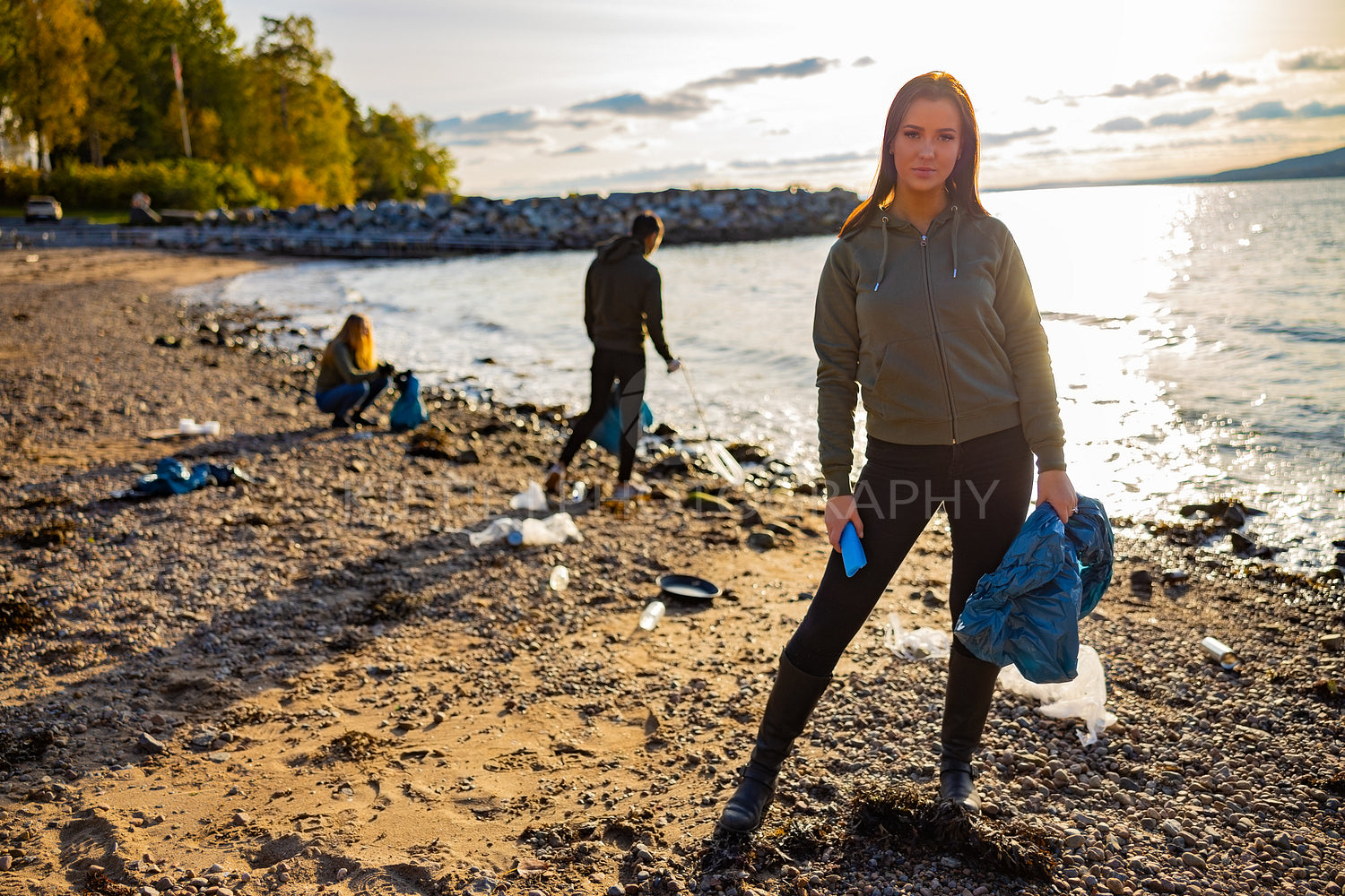 Serious young woman cleaning beach for plastic with volunteers during sunset