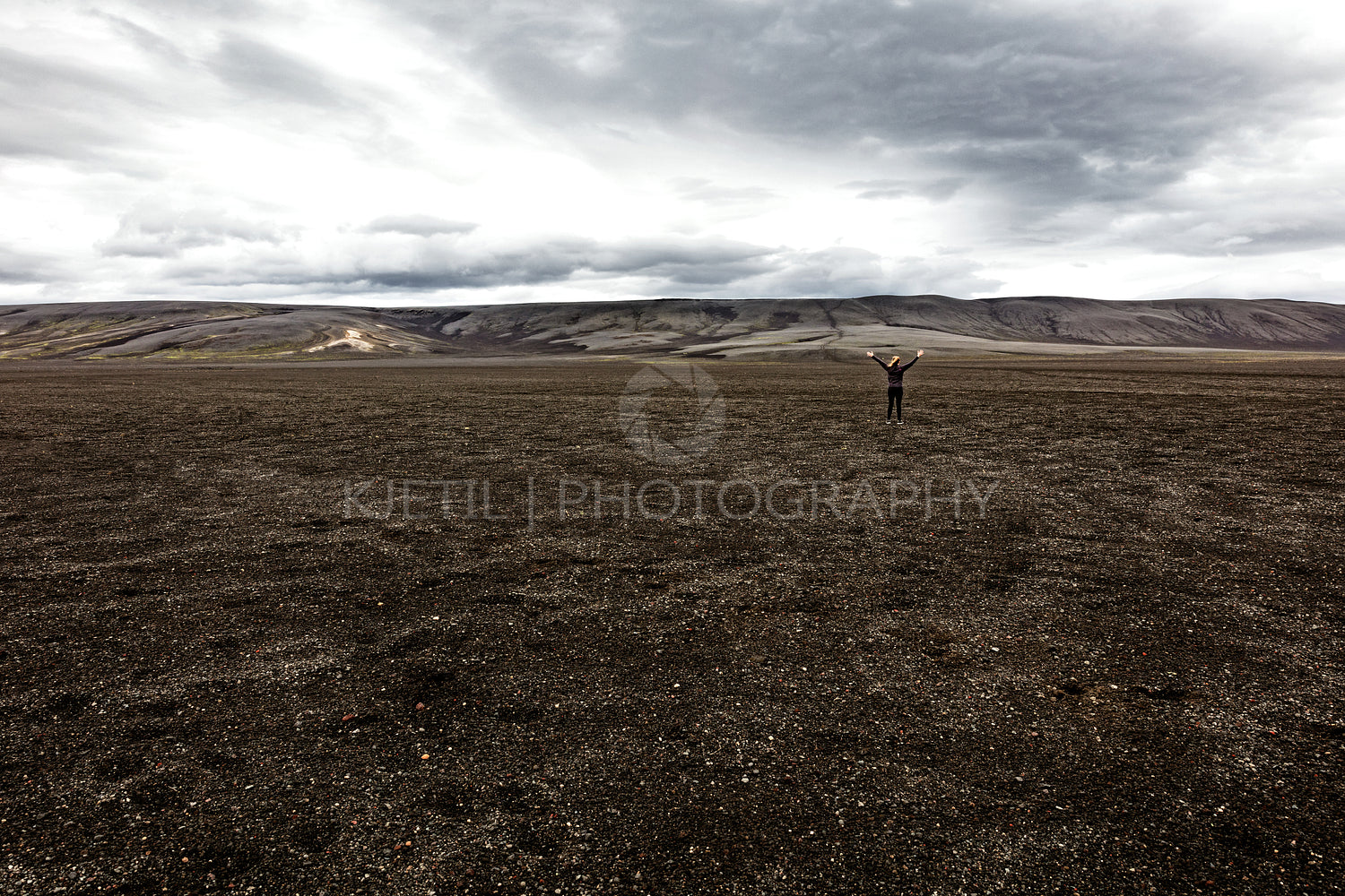 Hiker With Arms Raised Standing On Volcanic Landscape Against Sky