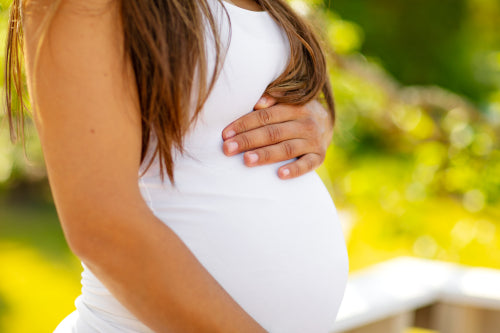 Mid-section of pregnant woman standing outdoor holding hands on belly