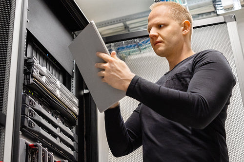 Male IT Technician Holding Digital Tablet Analyzing Servers in Datacenter