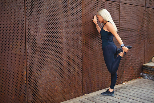 Back view of fit woman stretching after workout against metal wall in the city
