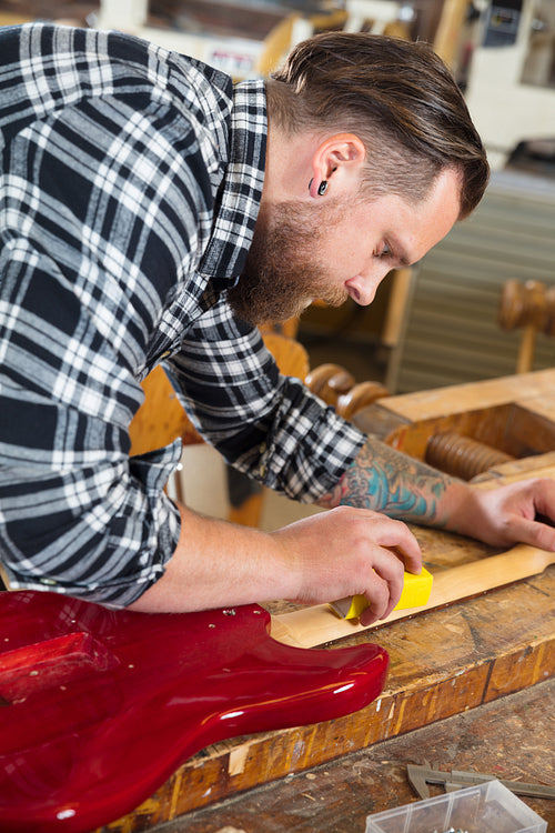 Craftsman sanding a guitar neck in wood at workshop