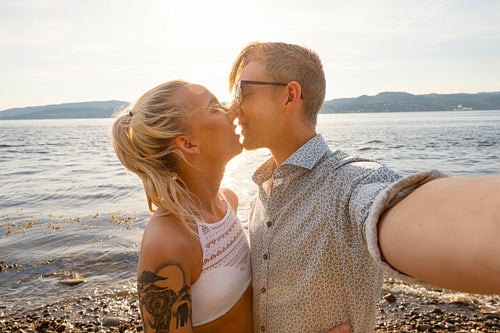 Happy Young Couple Kissing and Taking Selfie At Beach