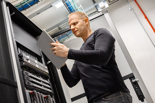 Male Technician Using Digital Tablet In Datacenter to Monitor SAN and Servers