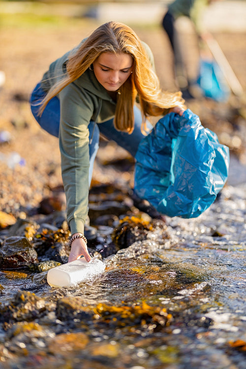 Young woman picking up garbage from rocky shore