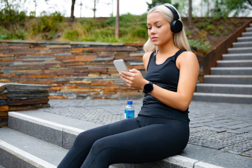 Beautiful sports woman sitting at stairs listen to music from smartphone