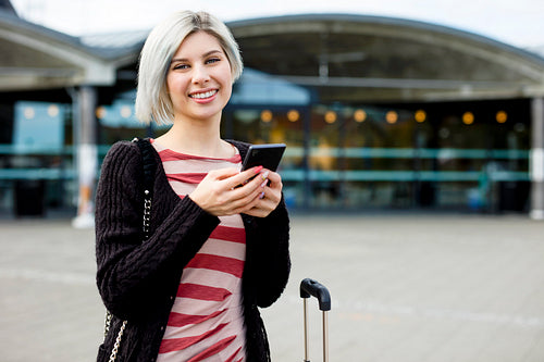 Smiling Female Traveler Using Smart Phone Outside Train Station