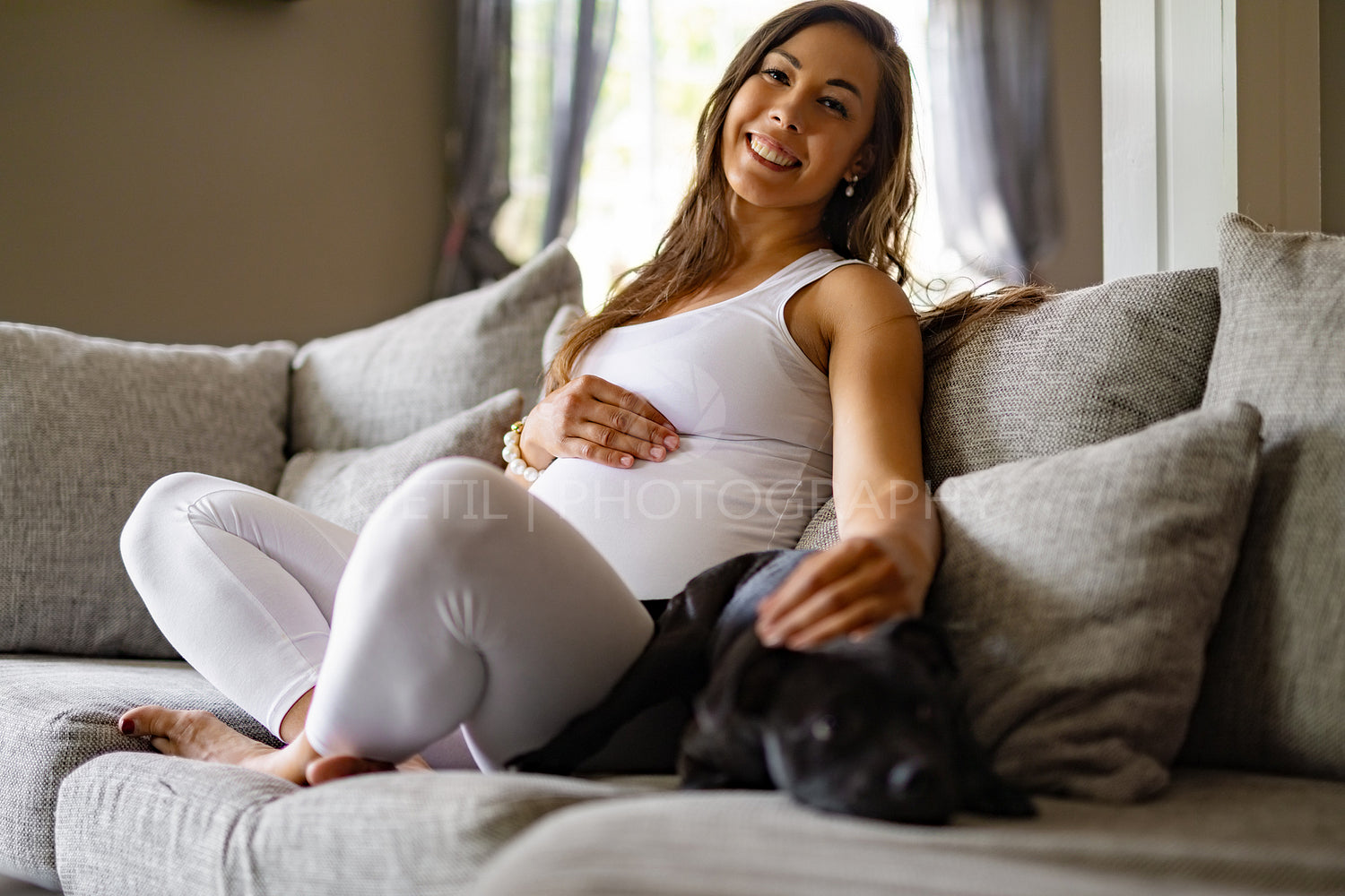 Happy pregnant woman sitting in sofa and pet her dog