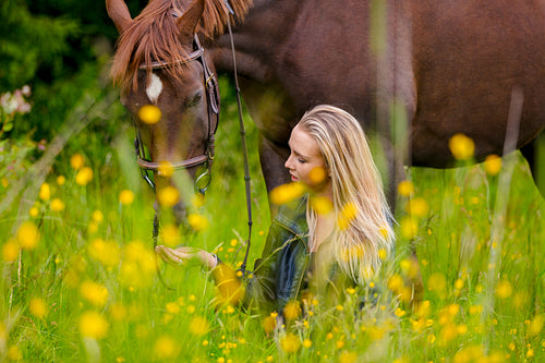 Woman sitting and talking in the meadow feeding her arabian horse