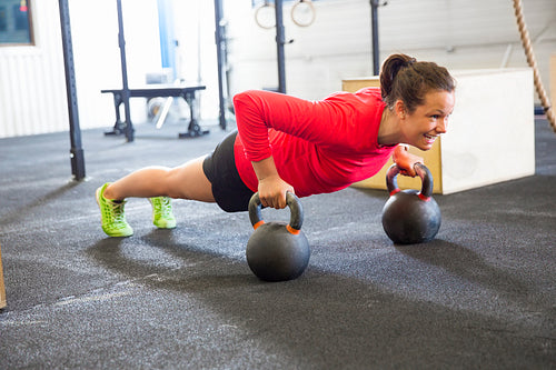 Determined Woman Doing Pushups On Kettlebell In Health Club