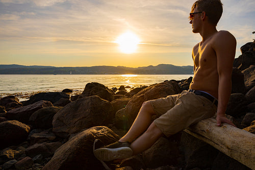 Young Shirtless Man Sitting On Rock During Sunset