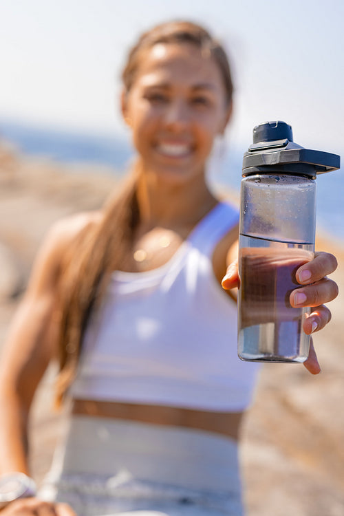 Smiling Female Holding Water Bottle After Exercising Outdoors