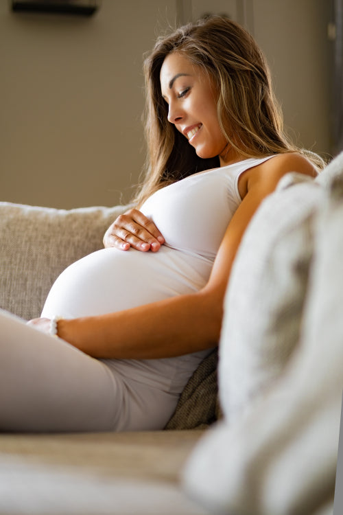 Smiling pregnant woman sitting in sofa looking at her stomach