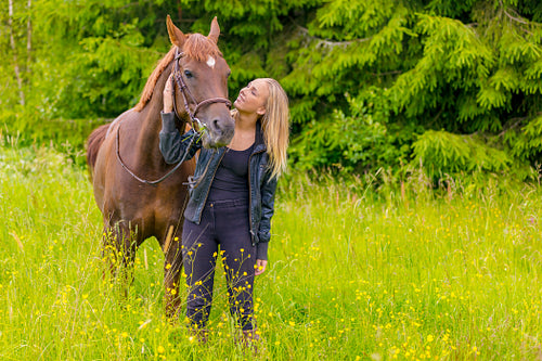 Smiling young woman feeding her arabian horse with snacks in the field