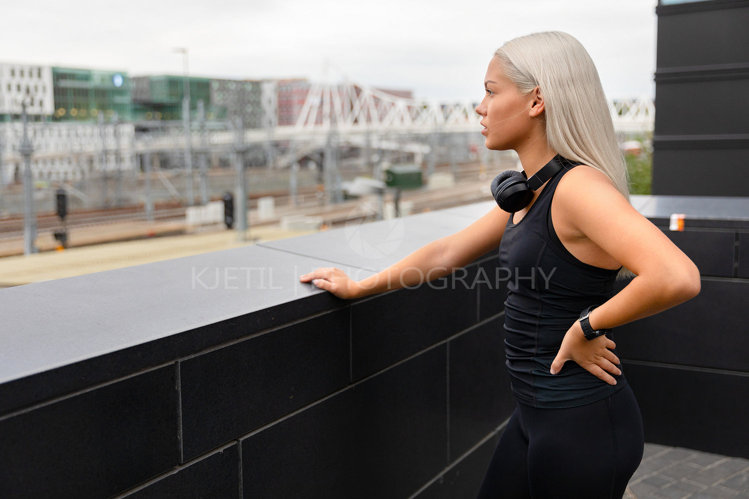 Fit Female Athlete with Headphones and Smartwatch Rests After Workout On Bridge