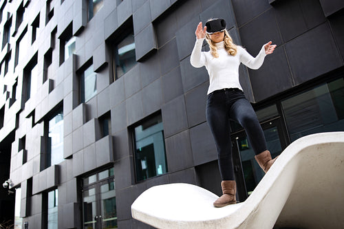 Blonde Woman Wearing Virtual Reality Glasses Against Futuristic Building