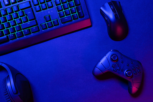 Green lit keyboard on blue lighted gaming gadgets on desk