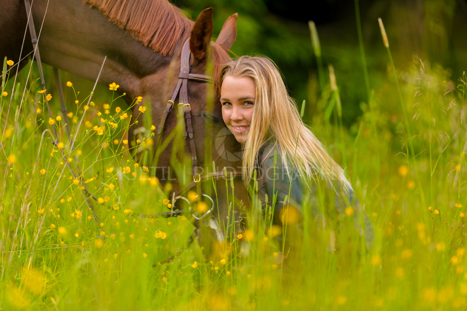 Smiling blonde woman sitting in the meadow with her arabian horse