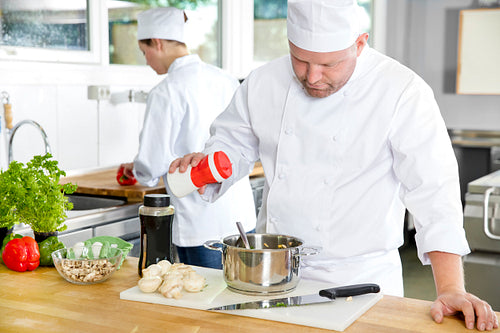 Two professional chefs preparing food in large kitchen