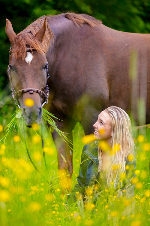 Smiling woman sits in the meadow with her arabian horse
