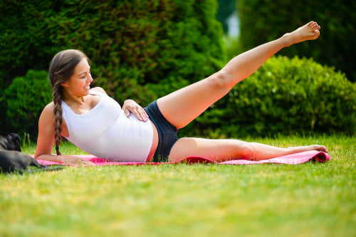 Pregnant Woman Performing Side Reclining Leg Lift In Park