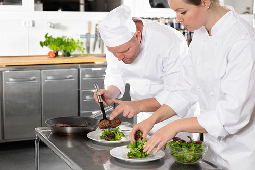 Two professional chefs prepares steak dish at gourmet restaurant