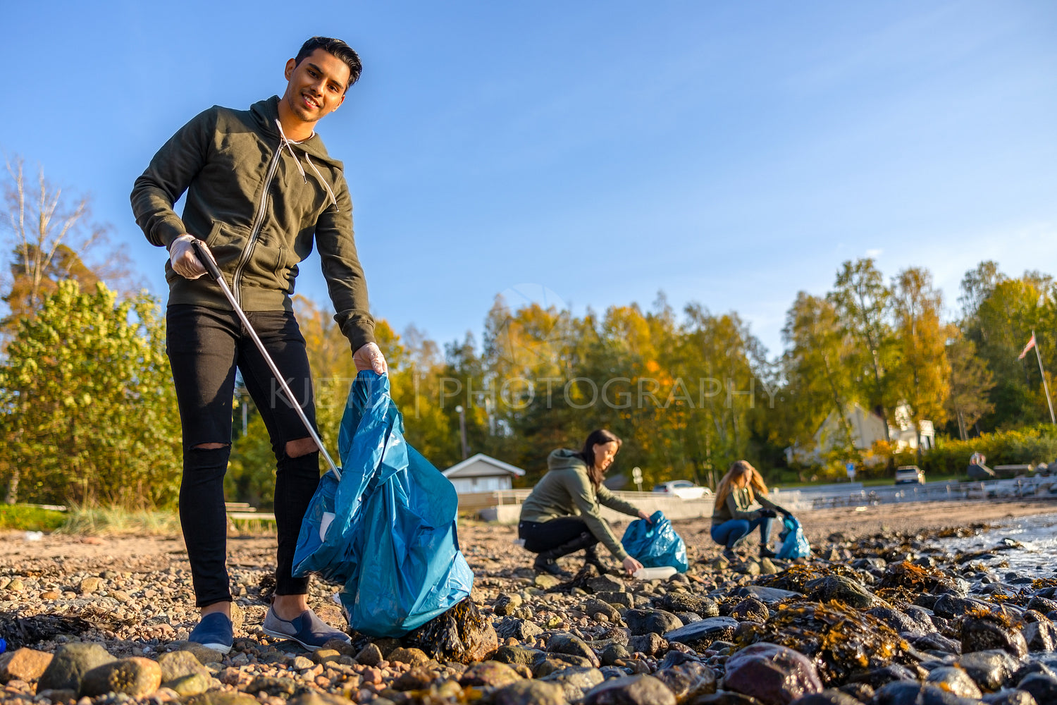Man cleaning beach with group of volunteers on sunny day