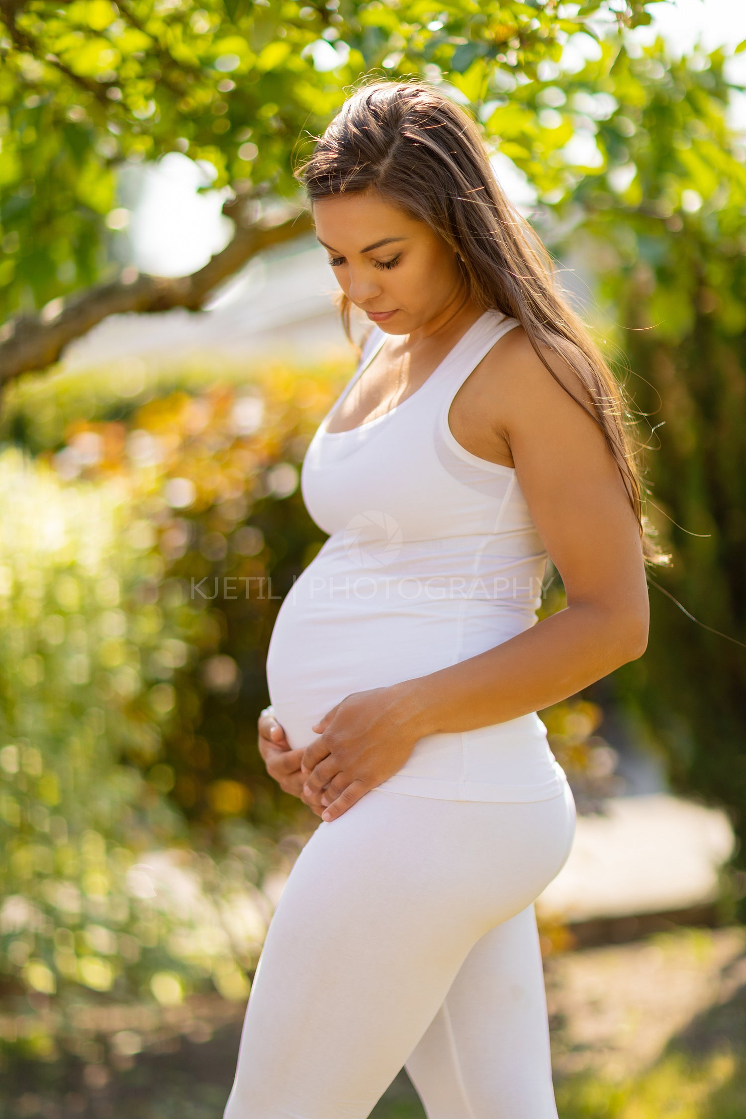 Pregnant woman standing in garden looking down at her belly