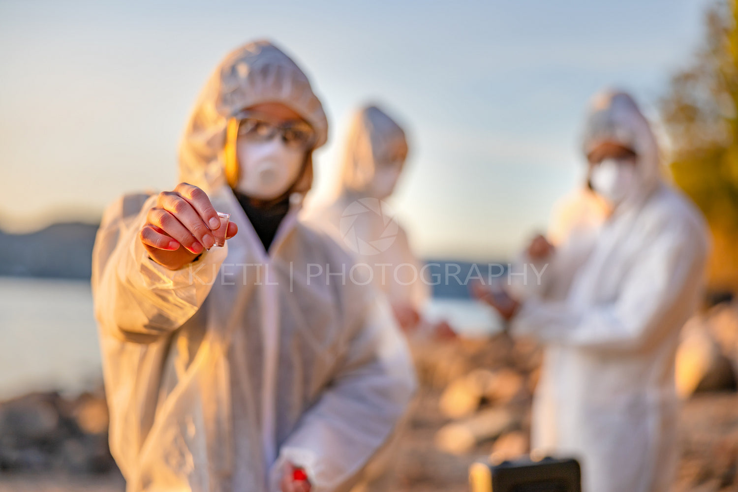 Scientist in white protective suit holding water sample at beach