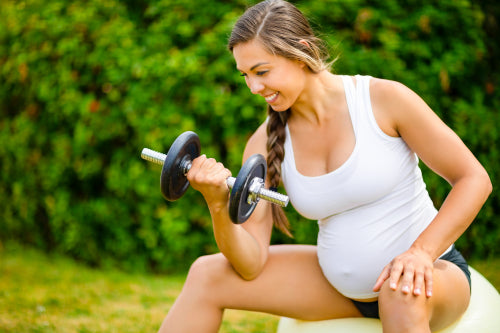 Pregnant Woman Lifting Dumbbells While Sitting On Exercise Ball