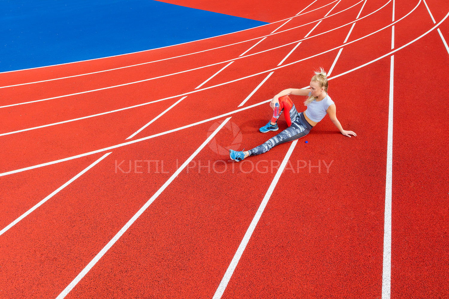 Athletic female runner rests on running track at sports arena