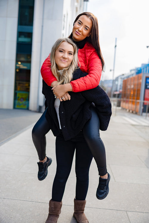 Smiling Female Friends Having Fun and Piggybacking In City