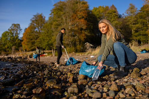 Focused young woman in environment conservation team picking up plastic at beach