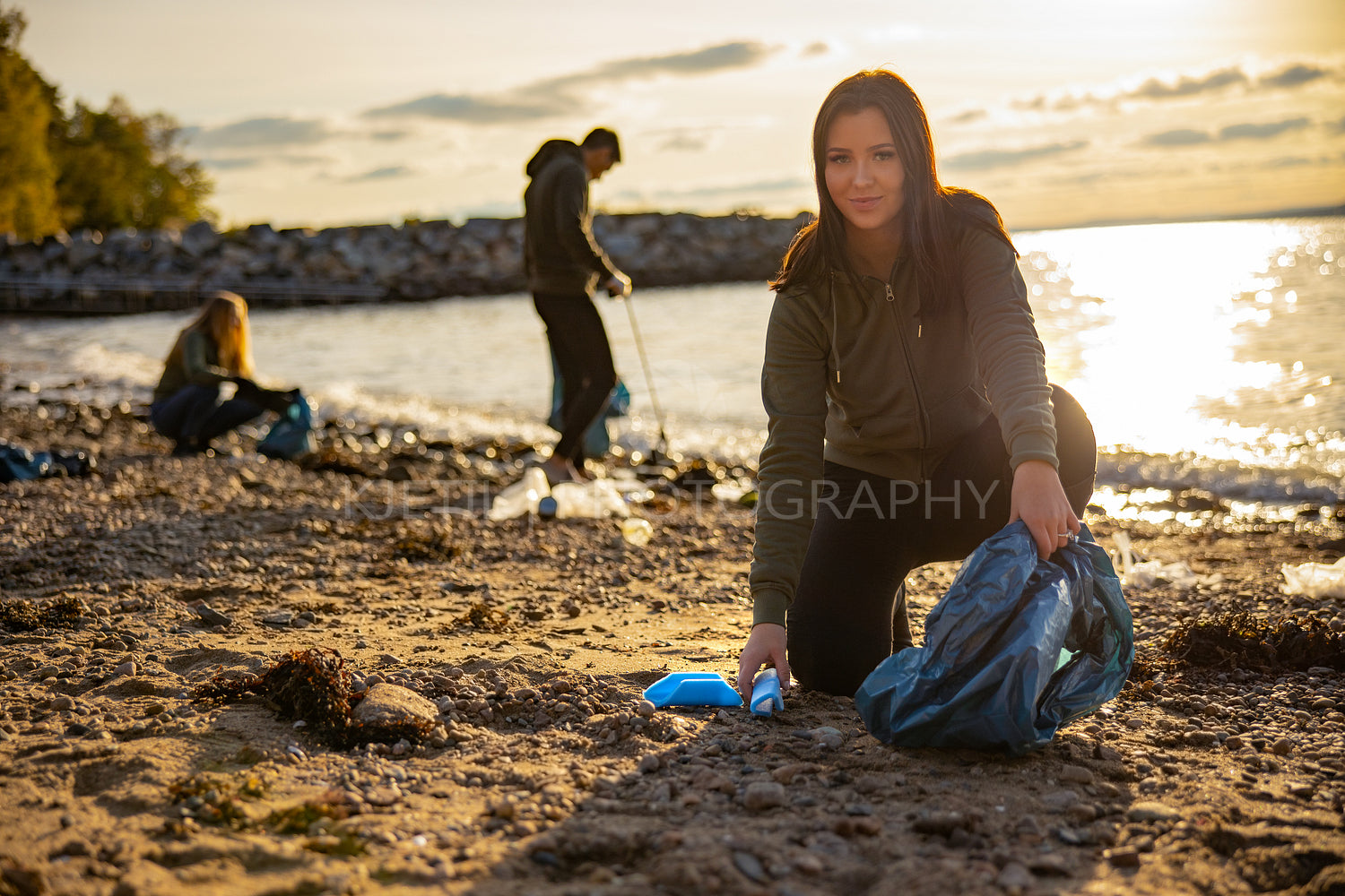Focused young woman cleaning beach with a team of volunteers during sunset