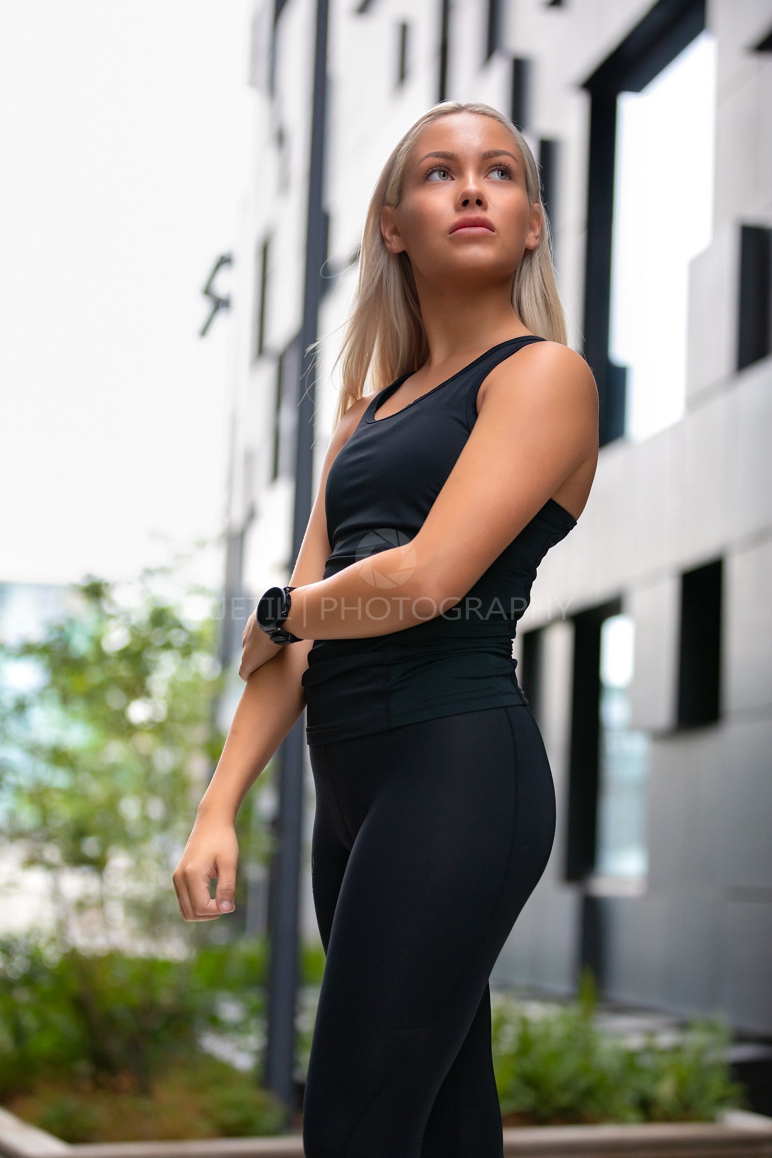 Young Woman in Workout Outfit Standing Against Futuristic Modern Building In City