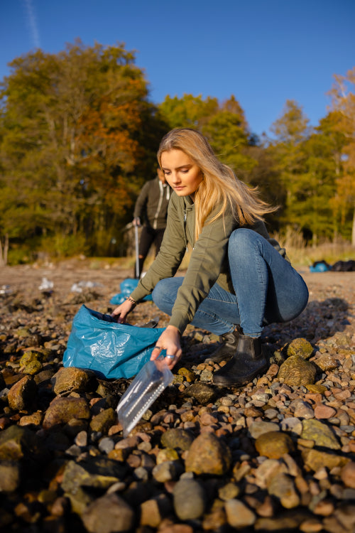 Young woman picking up plastic at rocky beach